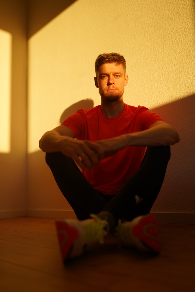 Taras, founder of BEATME, sitting against a sunlit wall in a red training shirt